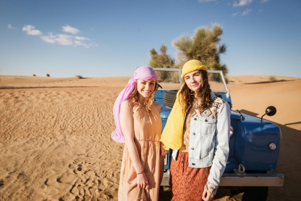 Two Women Standing In The Desert Beside A Blue Land Rover